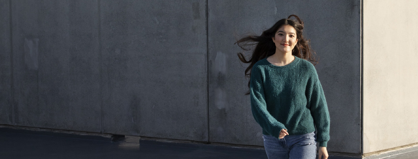 Female student walking outside happy grey walls